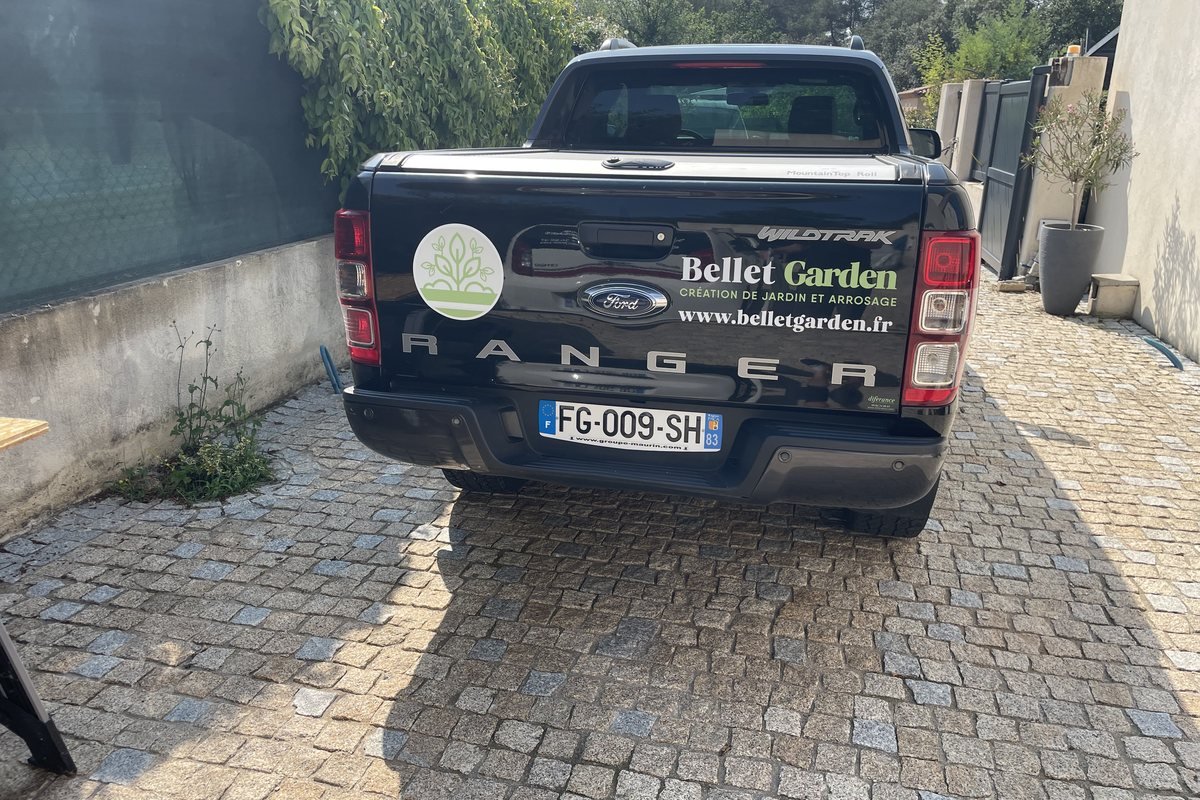 Pickup utilitaire d'un paysagiste marqué d'un logo et d'un lettrage adhésif sur la portière, garé devant un chantier